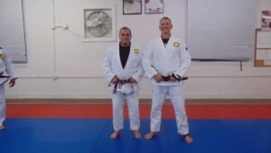 Two men in white uniforms standing on a blue mat.