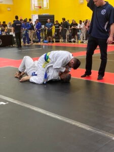 A man in white shirt and blue belt doing a judo move.