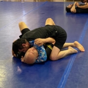 Two people are wrestling on a blue floor.