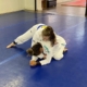 Two girls are practicing jiu jitsu on a blue floor.