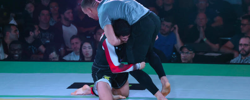 Two men are wrestling on a mat in front of an audience.