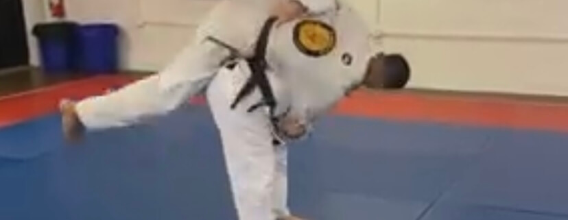 A man in white shirt and black belt doing a kick.