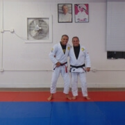 Two men in white uniforms standing on a blue mat.