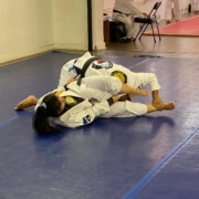 Two people are practicing jiu jitsu on a blue floor.