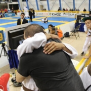 Two people hugging in a gym with other people watching.