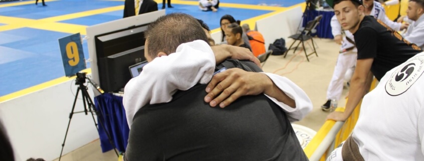Two people hugging in a gym with other people watching.
