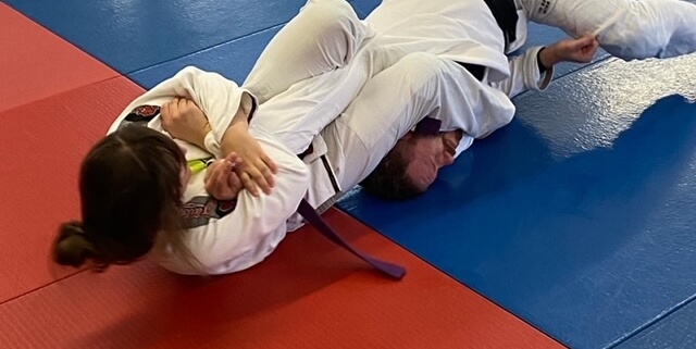 A woman is lying on the ground in a judo gym.