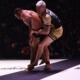 A man in yellow shorts and black shirt wrestling.
