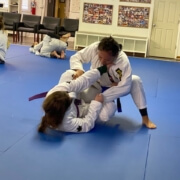 Two people practicing jiu jitsu on a blue mat.