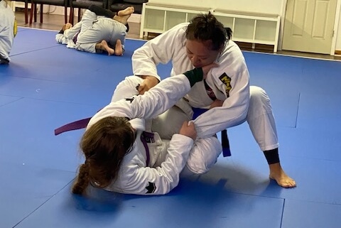 Two people practicing jiu jitsu on a blue mat.