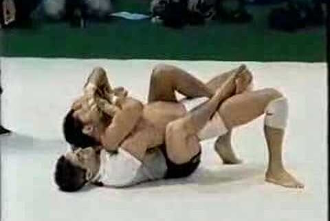 Two men are wrestling on a white mat.