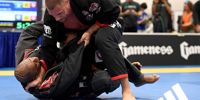 A man in black and red uniform on blue mat.